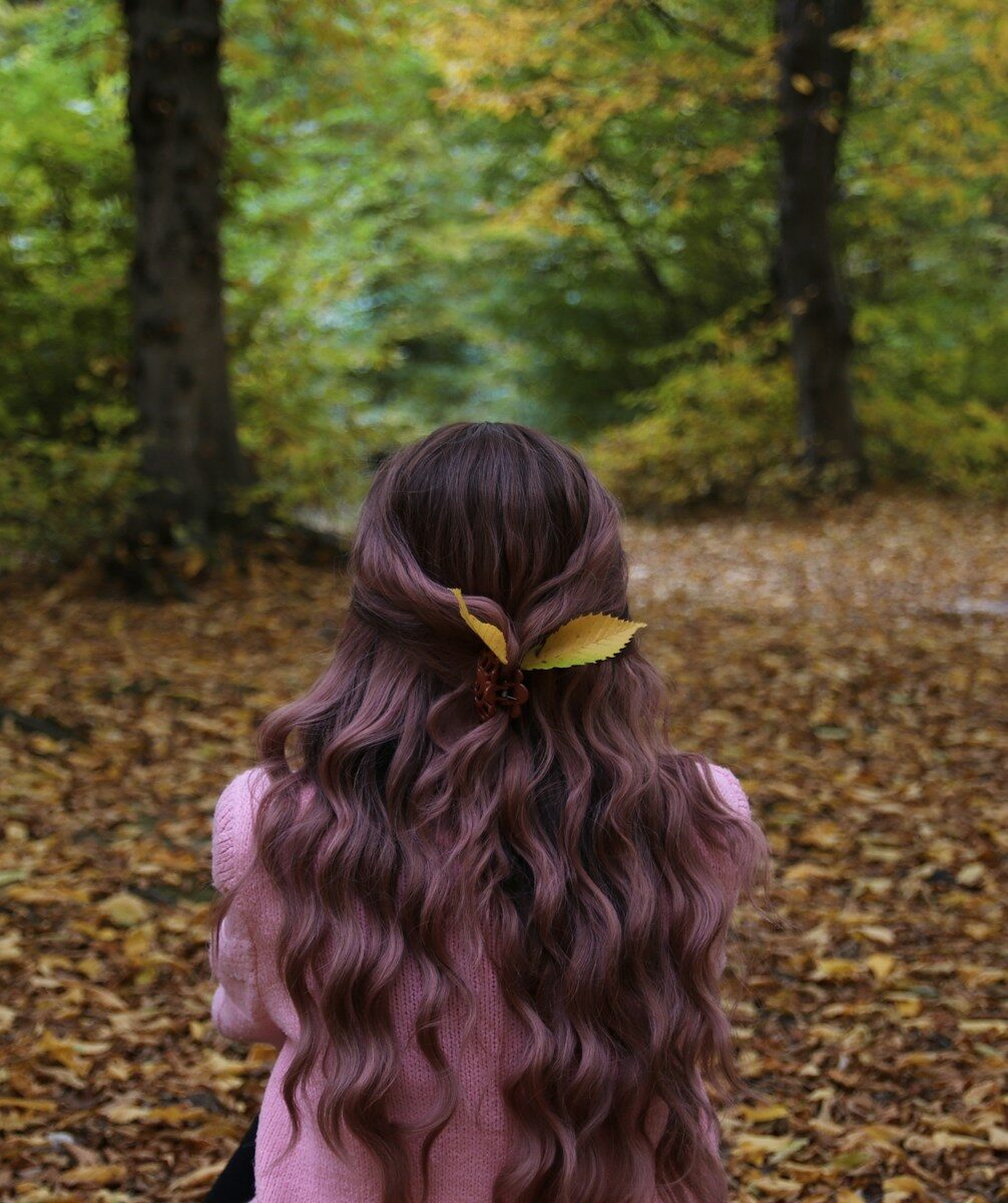 Photo by Nadiia Shuran a young girl with long curly hair sitting in the leaves